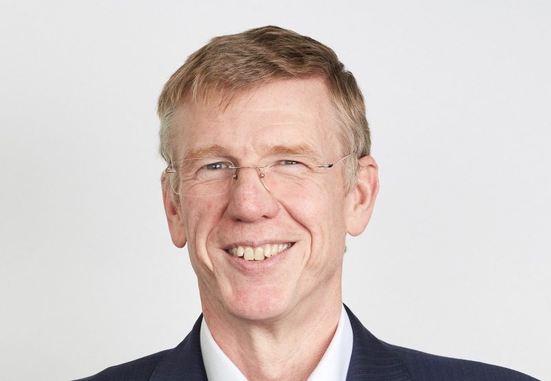 Head shot of Ken Cooper. He is wearing glasses and has a short haircut. You can see the top of his blue jacket and white collar.