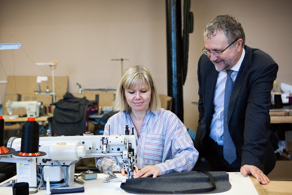 Woman sewing some material and man wearing suit watching her.
