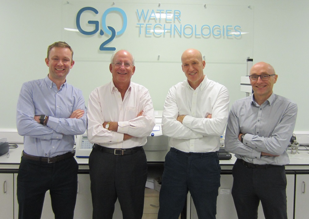 Four men standing together in front of G20 signage on wall.