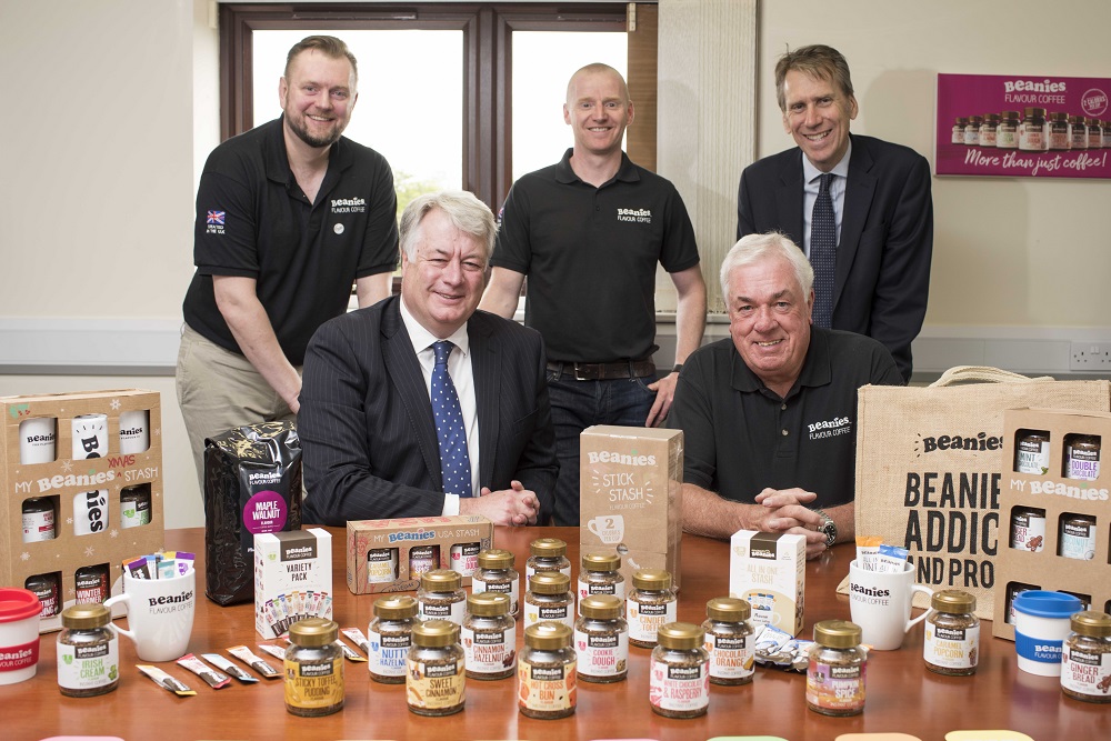 Five men in office, two sitting in front of desk surrounded by products and three men standing behind them.