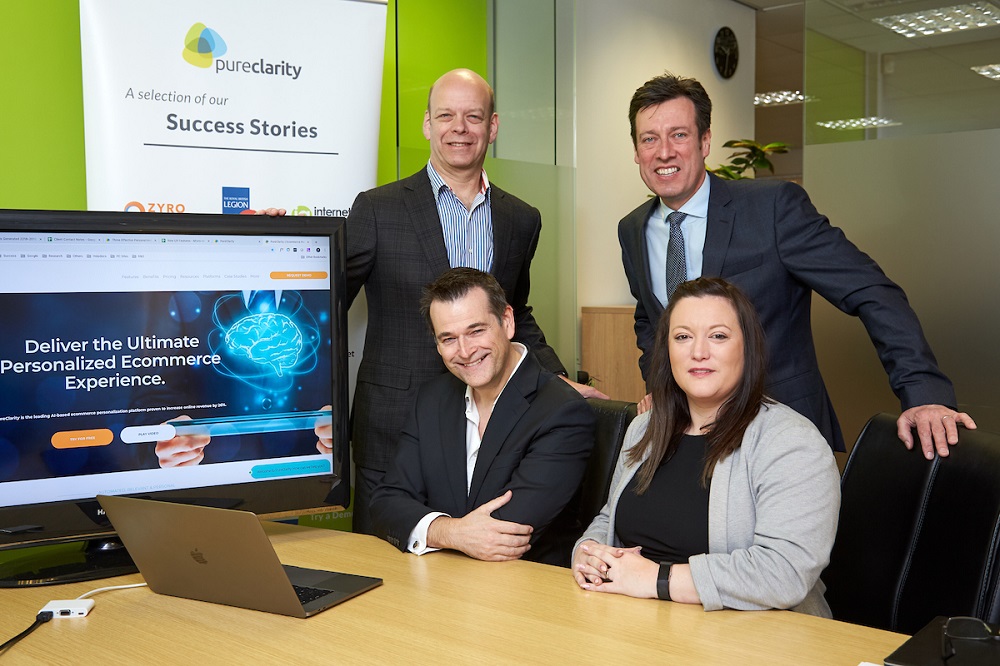 Three men and one woman in an office. Woman has dark long hair and grey jacket.