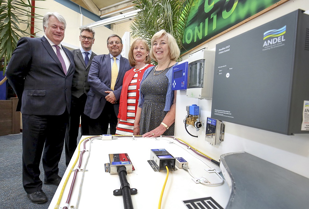Two woman to right in office and three men all wearing suits.